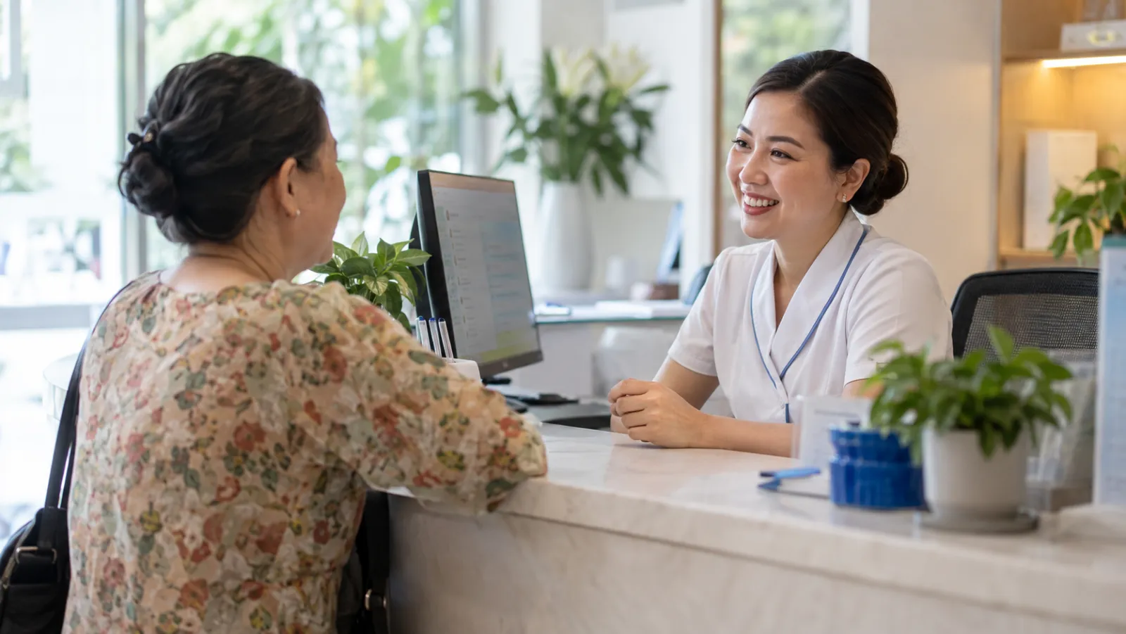 A clinic receptionist greeting a patient while a chat with another patient runs on her screen
